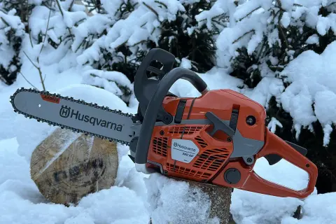 Pomarańczowa piła łańcuchowa Husqvarna 560 XP na tle zaśnieżonych drzew. Poznaj husqvarna 560 xp dane techniczne.