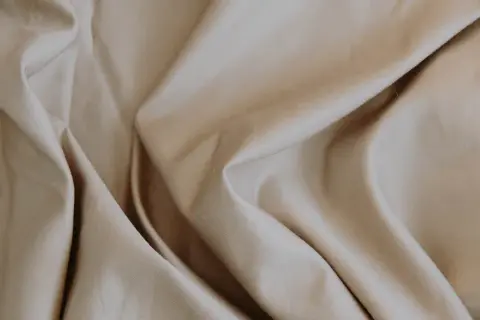Sanfter, beige Stoff fällt in weichen Falten. Lyocell ist das, ein nachhaltiges Material, das sich so angenehm anfühlt.