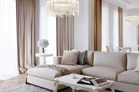 Elegancki salon w stylu modern classic z beżową sofą, kryształowym żyrandolem i jasnymi zasłonami.