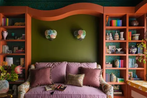 A cozy reading nook with a pink sofa, shelves filled with books and decor, and bright bold colors on the walls and shelving.