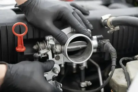 Mechanik w czarnych rękawiczkach sprawdza przepustnicę. Objawy jej awarii mogą być różne, np. nierówna praca silnika.