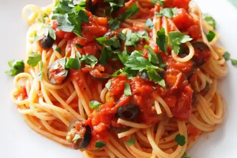 Pyszny makaron spaghetti z sosem pomidorowym, oliwkami i natką pietruszki. Czy makaron do spaghetti się płucze? Zazwyczaj nie, aby sos lepiej przylegał.