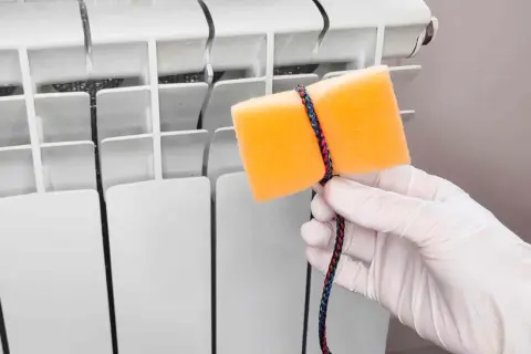 Guanto bianco e spugna arancione legata con cordino colorato, pronti per pulire i termosifoni.