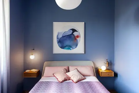 Camera da letto con pareti blu intenso e un quadro astratto. Letti con cuscini rosa e una coperta viola creano colori rilassanti.