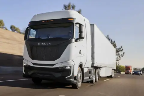 Le Nikola One, un camion blanc futuriste, roule sur l'autoroute sous un ciel bleu clair.