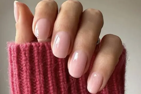 Delikatne, różowe paznokcie w stylu "soap nails" lśnią na tle grubego, różowego swetra.