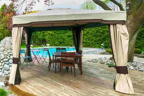 Gazebo su terrazza in legno, con tavolo e sedie, vicino a una piscina. Soluzione per come fissare un gazebo su terrazza senza bucare il pavimento.