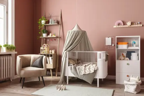Une chambre de bébé chaleureuse avec un lit à baldaquin, une chaise confortable et des étagères pleines de jouets. Parfait pour une diy déco chambre bébé.