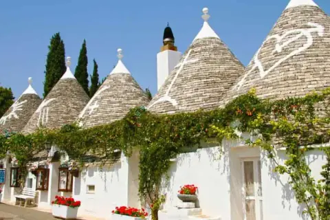 I trulli di Puglia, con i loro tetti conici e le decorazioni bianche, incantano sotto il cielo azzurro, avvolti dal verde rampicante.