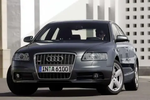 Elegancki, ciemnoszary Audi A6 C6 z przyciemnianymi szybami i chromowanymi felgami, zaparkowany przed nowoczesnym budynkiem.