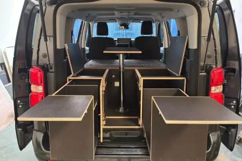 Soluciones de trucos almacenaje furgonetas camper: módulos de madera con compartimentos y mesa abatible para maximizar el espacio.
