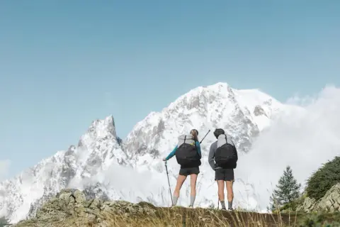 Deux randonneurs, prêts pour une randonnée de 3 jours, contemplent un paysage montagneux enneigé sous un ciel bleu.