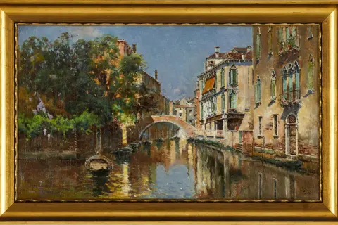 Un canal veneciano con un puente de arco, barcas y edificios históricos, pintado por Antonio Reyna Manescau.
