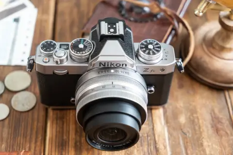 Un appareil photo Nikon Zfc argenté et noir, prêt pour un avis. Des pièces et des billets sont à côté.