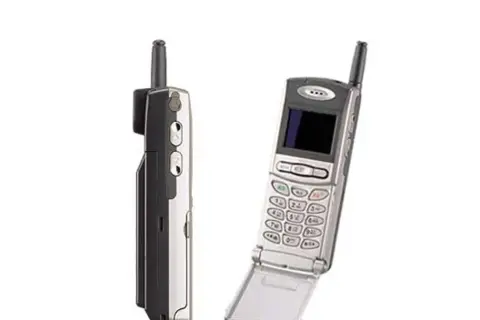Dwa stare telefony komórkowe, jeden z nich to prawdopodobnie pierwszy telefon z aparatem, z charakterystyczną antenką i klapką.