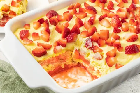 Tiramisù fragole in una teglia bianca, con strati di crema, biscotti e tante fragole fresche a pezzi.
