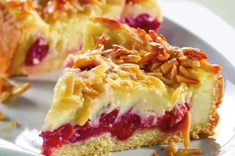 Ein Stück von Omas Kirschkuchen mit Pudding, belegt mit Mandelblättchen. Saftige Kirschen und cremiger Pudding unter knuspriger Kruste.