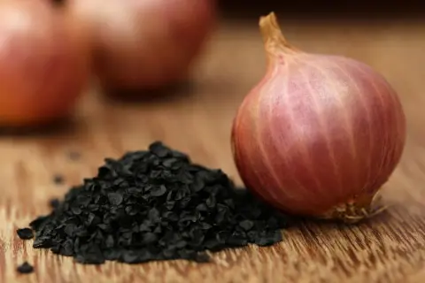 Kupa czarnych nasion cebuli obok czerwonej cebuli.