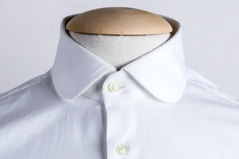 Dettaglio di una camicia bianca con colletto arrotondato, uno dei tanti tipi di colletto camicia, su un manichino.