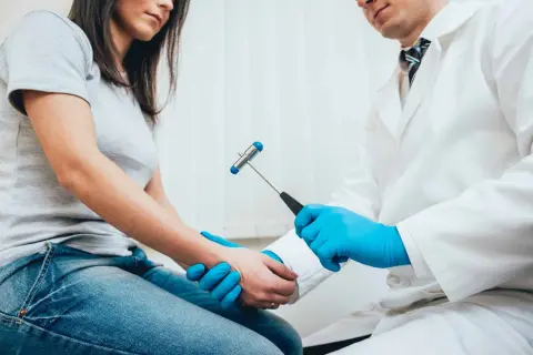 Neurolog bada odruchy pacjentki młoteczkiem neurologicznym.