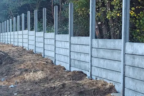 Wykończenie słupów zewnętrznych w postaci betonowego muru oporowego, budowanego z prefabrykowanych elementów, z widocznym terenem budowy.