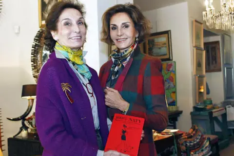 Naty Abascal y otra mujer posan con un libro rojo titulado "100% NATY".