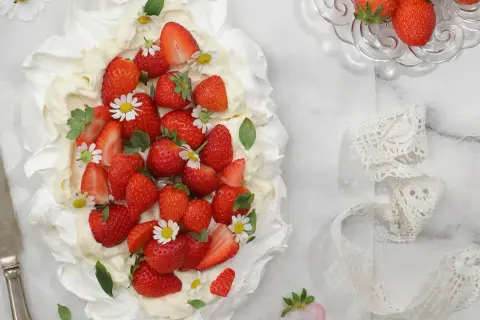 En vacker pavlova med vispgrädde och massor av saftiga jordgubbar, dekorerad med små vita blommor. Perfekt för en somrig fika.