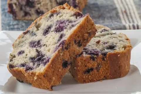 Szybkie i proste ciasto z jagodami, pokrojone na kromki, leży na białym talerzu.
