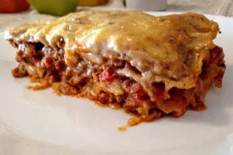 Kawałek zapieczonej lasagne z ciągnącym się serem na białym talerzu.