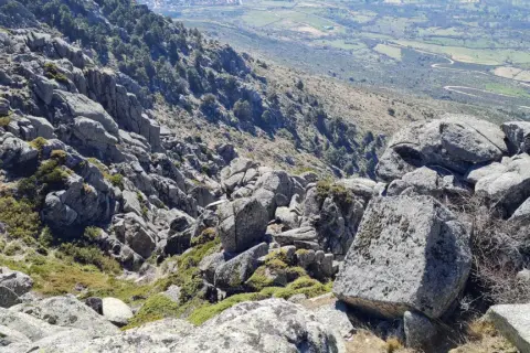 Rocas y vegetación en el cancho del águila, con un valle verde y camino serpenteante al fondo.