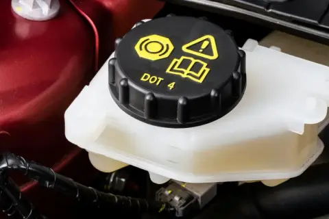 Le réservoir de liquide de frein est visible, avec le bouchon noir marqué "DOT 4". Le niveau du liquide est bien visible dans le récipient translucide.