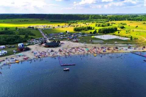 Tętniące życiem jezioro koło Wrocławia. Plaża pełna ludzi, namiotów i kamperów, z wodą i zielonymi polami w tle.