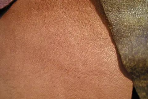 Texture d'un cuir d'agneau plongé, d'une teinte rosée, contrastant avec un cuir plus sombre et rugueux.