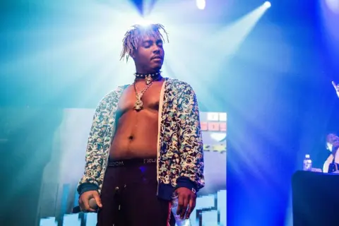 Juice WRLD on stage, a testament to his massive Juice WRLD Spotify streams. The artist, bathed in blue light, holds a microphone and a bottle.