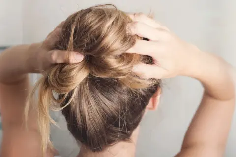 Hände formen einen unordentlichen Dutt, eine von vielen leichten Frisuren für den Alltag.