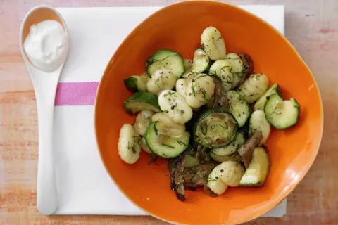 Gnocchi mit Zucchini und Pilzen in einer orangen Schüssel, dazu ein Löffel cremiger Dip. Eine köstliche zucchini pfanne.