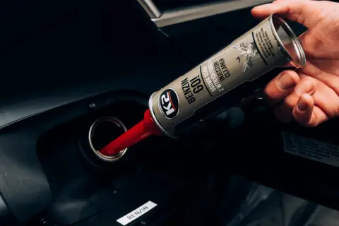 Dłoń wlewa dodatek do benzyny z puszki do baku samochodu. Produkt czyści wtryskiwacze.