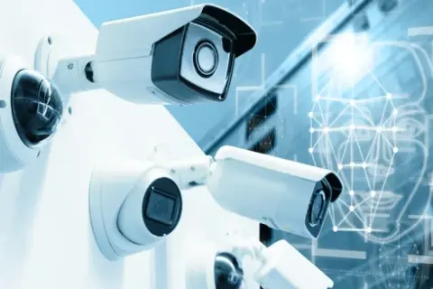 Plusieurs caméras de surveillance sont montées sur un mur blanc. En arrière-plan, un visage stylisé avec des points connectés suggère la technologie de caméra ai.