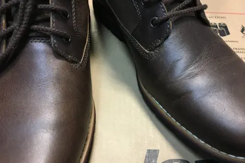Brązowe, skórzane buty z ciemnymi sznurówkami. Skóra na jednym bucie jest lekko pognieciona, co może sugerować potrzebę dowiedzenia się, jak wyprostować skórę na butach.