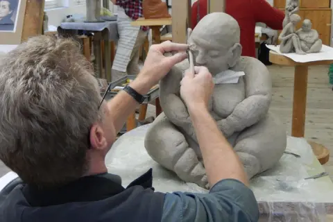 Ein Künstler formt mit Werkzeug eine Tonfigur in einem Atelier.