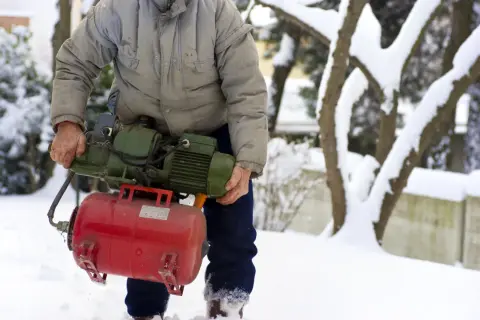 Mężczyzna w zimowej scenerii trzyma pompę, przygotowując się do zadania, jak wypompować wodę ze zbiornika na deszczówkę.