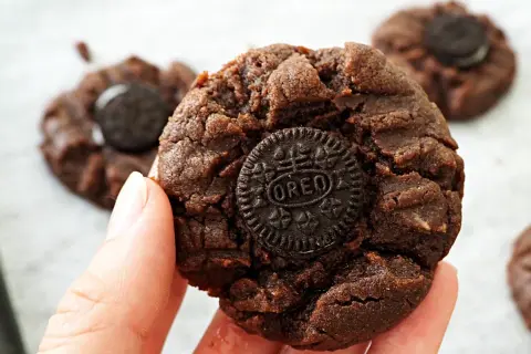 En hand håller en chokladkaka med en Oreo-kaka i mitten. Flera liknande nutella kakor syns i bakgrunden.