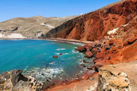 Santorini plaże: turkusowe morze obmywa czerwoną, wulkaniczną plażę, otoczoną skalistymi klifami.