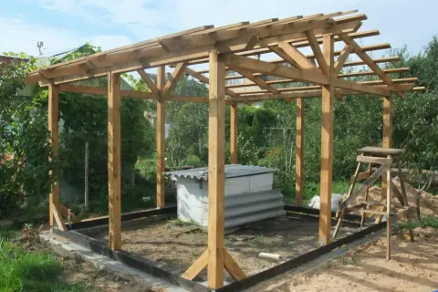 Trwa budowa projektu altany ogrodowej. Drewniana konstrukcja z dachem w trakcie prac. W środku biała skrzynia.