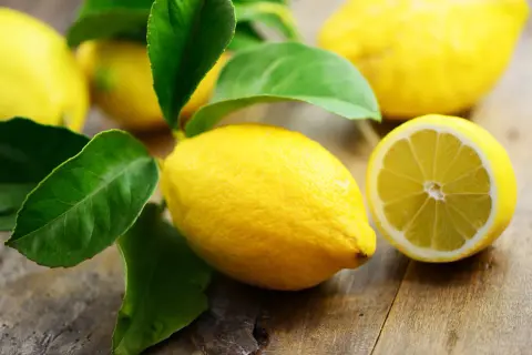 Frische Zitronen mit grünen Blättern auf Holz. Eine Zitrone ist halbiert. Interessant, wieviel Vitamin C hat eine Zitrone?