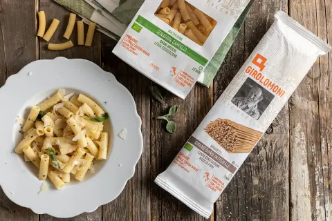 Piatto di maccheroni conditi e pacchi di pasta della Gino Girolomoni Cooperativa Agricola, con grano italiano.