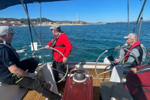 Uomini imparano a navigare durante un corso skipper, con un istruttore che guida il timone.