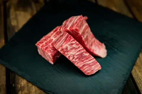 Drei Stücke erstklassiges Kobe Rindfleisch mit feiner Marmorierung liegen auf einem dunklen Stein.