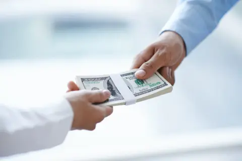 Przekazanie pliku banknotów dolarowych. Zastanawiasz się, do jakiej kwoty można płacić gotówką?