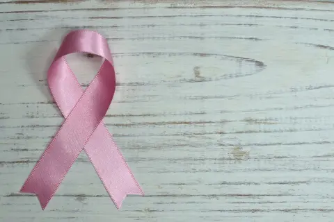 Różowa wstążka na białym, drewnianym tle. Symbol nadziei i wsparcia, przypominający o mądrych słowach otuchy w chorobie.